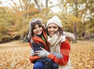 Madre e hija sonriendo en hojas de otoño - foto de stock