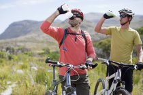 Ciclistas de montaña que conducen agua en el paisaje rural - foto de stock