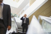 Hombre de negocios hablando por teléfono celular en la parte superior de las escaleras en el edificio de oficinas - foto de stock
