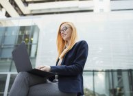 Geschäftsfrau arbeitet am Laptop vor Bürogebäude — Stockfoto
