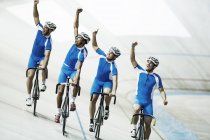 Equipo de ciclismo de pista cabalgando en velódromo con los brazos levantados - foto de stock