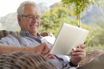 Uomo anziano sorridente utilizzando tablet digitale sul patio — Foto stock