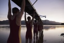 Rowing team carrying boat overhead into lake — Stock Photo