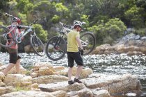 Hombres que llevan bicicletas de montaña en la formación de rocas - foto de stock