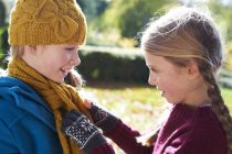 Girl tying sisters scarf outdoors — Stock Photo