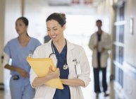 Doctor looking down at files in hospital corridor — Stock Photo