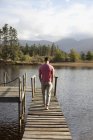Man walking along dock over lake — Stock Photo