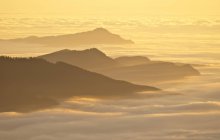 Vista aérea dos cumes das montanhas sobre as nuvens ao pôr do sol — Fotografia de Stock