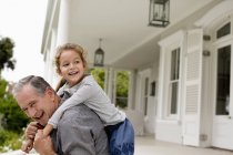Older man carrying granddaughter piggy back on porch — Stock Photo