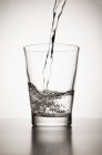 Água derramando em vidro no fundo branco — Fotografia de Stock