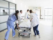 Doctors rushing patient on stretcher down hospital corridor — Stock Photo