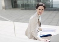 Porträt einer lächelnden Geschäftsfrau mit Laptop und Papierkram vor dem Gebäude — Stockfoto