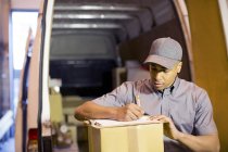 Delivery boy writing on clipboard in van — Stock Photo