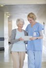 Медична сестра та старіння пацієнта читають таблицю в лікарняному коридорі — стокове фото