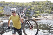 Uomo che trasporta mountain bike nel fiume — Foto stock