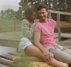 Улыбающаяся пара, сидящая на пристани над озером — стоковое фото