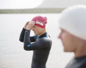 Confident and strong triathletes pulling on goggles on beach — Stock Photo