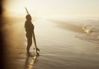 Серфер, стоящий с доской на пляже — стоковое фото