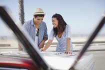 Lächelndes Paar liest Straßenkarte auf Cabrio — Stockfoto