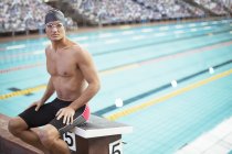 Swimmer sitting on starting block at poolside — Stock Photo