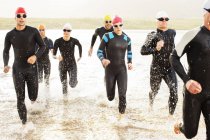Confident and strong triathletes in wetsuits walking in waves — Stock Photo