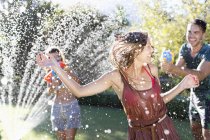 Adult friends playing with water guns in sprinkler — Stock Photo