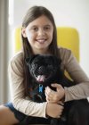 Sonriente chica sosteniendo perro en casa moderna - foto de stock