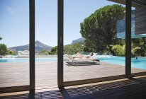 Bain de soleil femme sur chaise longue à côté de la piscine de luxe avec vue sur la montagne — Photo de stock