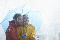 Feliz pareja caucásica bajo paraguas bajo la lluvia - foto de stock