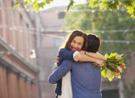 Smiling woman with flowers hugging man — Stock Photo