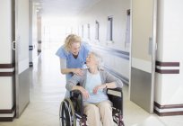 Медсестра зі старінням пацієнта в інвалідному візку в лікарняному коридорі — стокове фото