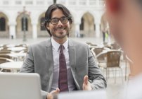 Smiling businessman talking to co-worker at sidewalk cafe — Stock Photo