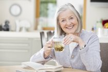Older woman drinking tea and reading — Stock Photo