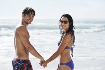 Retrato de pareja feliz cogida de la mano en la playa - foto de stock