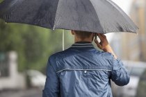 Man talking on cell phone under umbrella in rain — Stock Photo