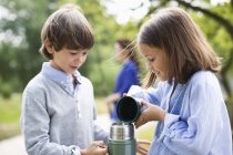 Crianças derramando chá de garrafa térmica ao ar livre — Fotografia de Stock