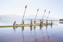 Squadra canottaggio con remi sollevati sul lago — Foto stock