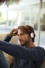 Jeune homme attrayant écoutant des écouteurs sur le canapé — Photo de stock