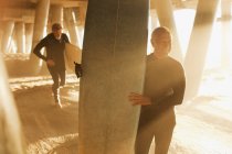 Vecchi surfisti che trasportano tavole sotto il molo — Foto stock