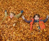 Niños felices acostados en hojas de otoño - foto de stock