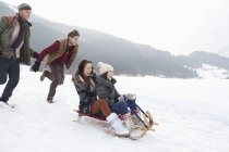 Amigos entusiastas paseando en trineo en el campo nevado - foto de stock
