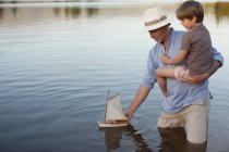 Дедушка и внук плывут по озеру с игрушечным парусником — стоковое фото