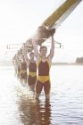 Rowing team carrying scull overhead in lake — Stock Photo