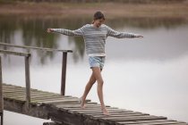 Woman walking on dock over lake with arms outstretched — Stock Photo