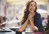 Усміхнена жінка п'є каву в тротуарному кафе — стокове фото