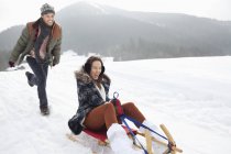 Enthusiastic couple sledding in snowy field — Stock Photo