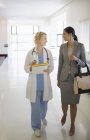 Médico y mujer de negocios caminando en el pasillo del hospital - foto de stock