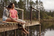 Sereno casal sentado na borda da doca sobre o lago — Fotografia de Stock