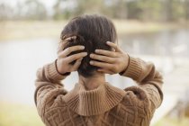 Visão traseira da mulher com o cabelo nas mãos à beira do lago — Fotografia de Stock
