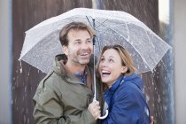 Happy couple under umbrella in downpour — Stock Photo